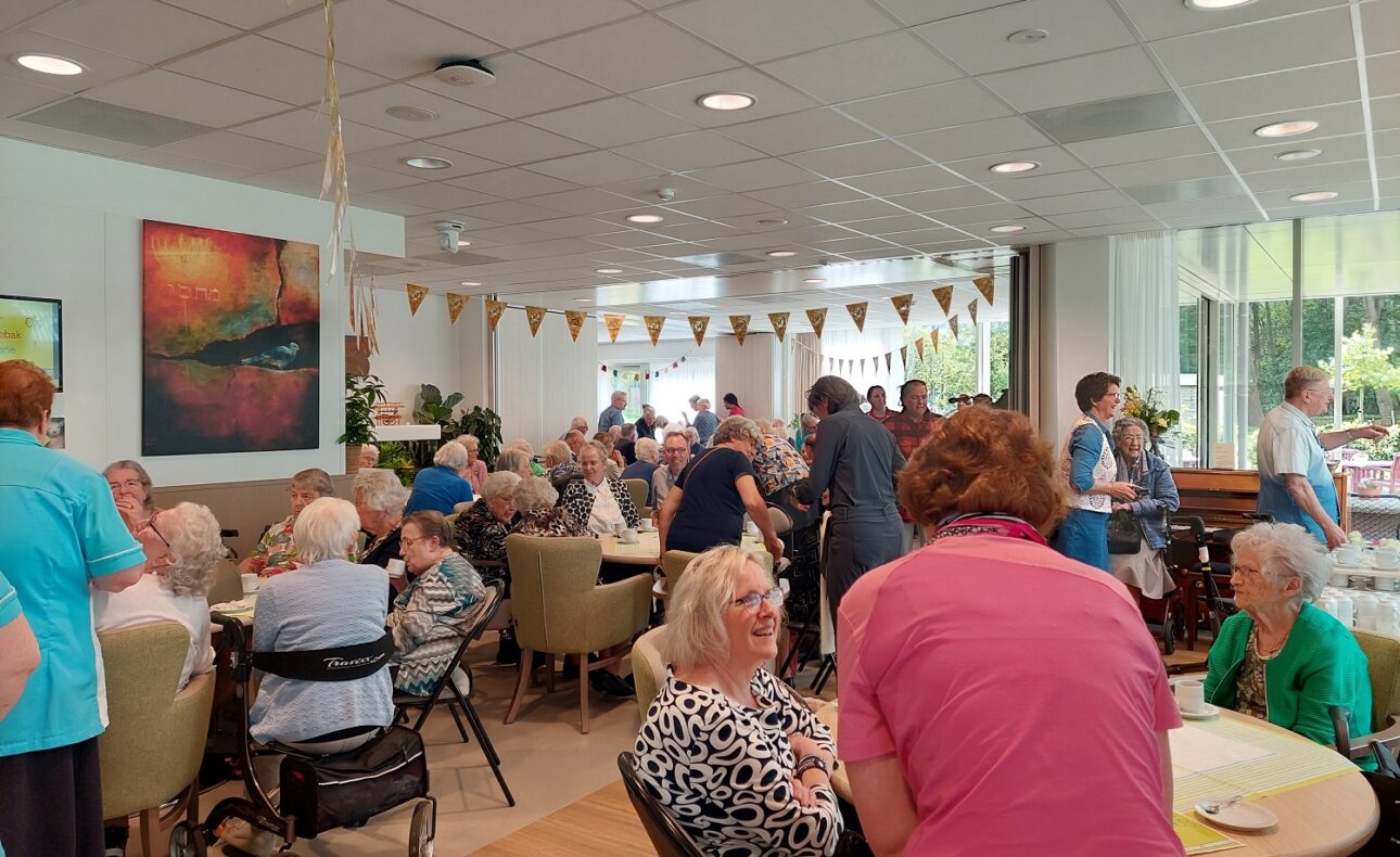 Groep mensen viert een feestelijke dag in een gemeenschappelijke ruimte met slingers en schilderijen aan de muur.