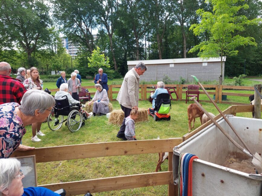 Groep mensen, waaronder ouderen en kinderen, geniet van een zonnige dag buiten met dieren in een groene omgeving.