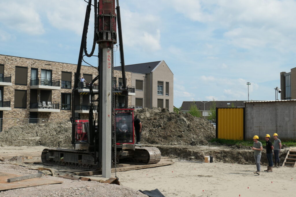 Bouwplaats met een heistelling en drie bouwvakkers in gesprek. Op de achtergrond zijn moderne appartementen te zien.
