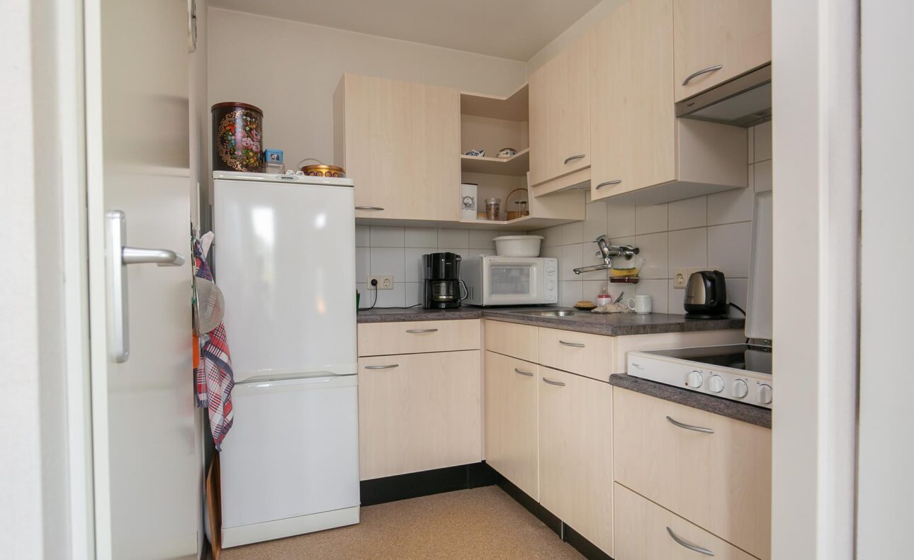 Keuken met lichte houten kasten, een witte koelkast, magnetron, koffiezetapparaat en waterkoker op het aanrecht.