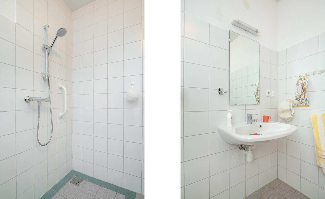 Afbeelding van een badkamer met een douche aan de linkerkant en een wastafel met spiegel aan de rechterkant, beide met witte tegels.