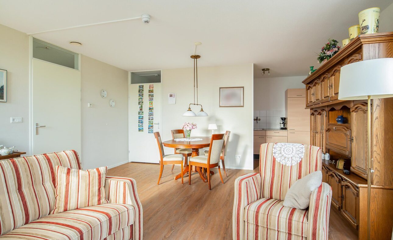 Woonkamer met gestreepte banken, houten eettafel met stoelen, hanglamp en houten kast. Heldere en gezellige sfeer.