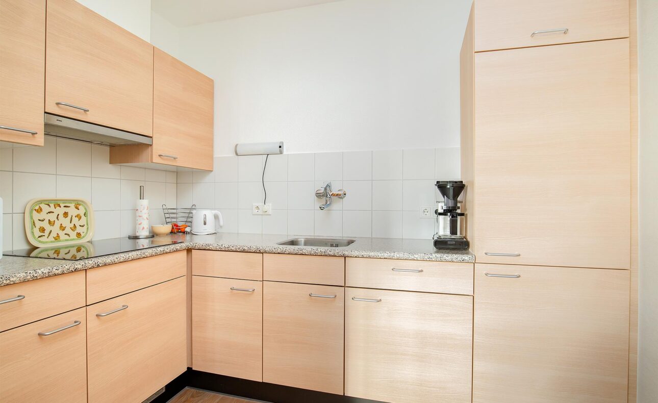Keuken met houten kasten, een gootsteen, koffiezetapparaat en een tegelachterwand. Er staat een broodrooster op het aanrecht.