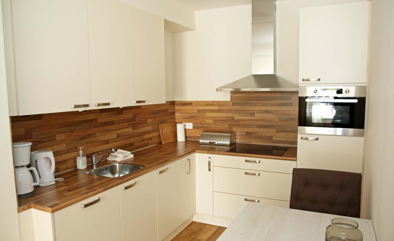 Moderne keuken met witte kasten, houten werkblad, ingebouwde oven, afzuigkap, koffiezetapparaat en spoelbak.