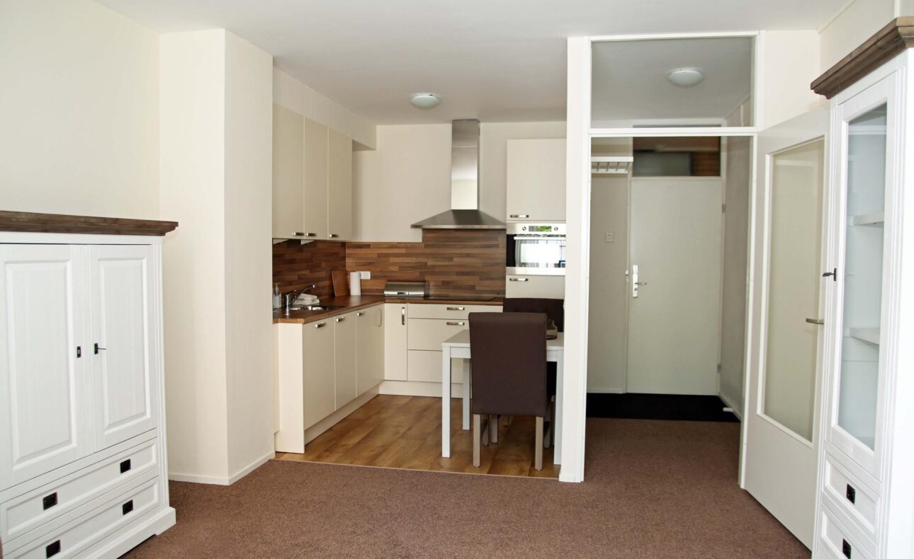 Afbeelding van een moderne keuken met witte kasten, een houten aanrechtblad en een kleine eettafel met twee stoelen.