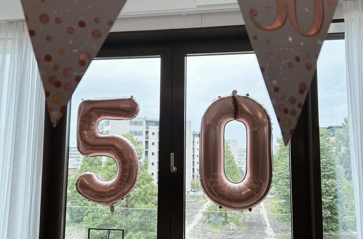 Vlaggen en ballonnen met het getal 50 hangen voor een raam, ter viering van een 50e verjaardag in een kamer.