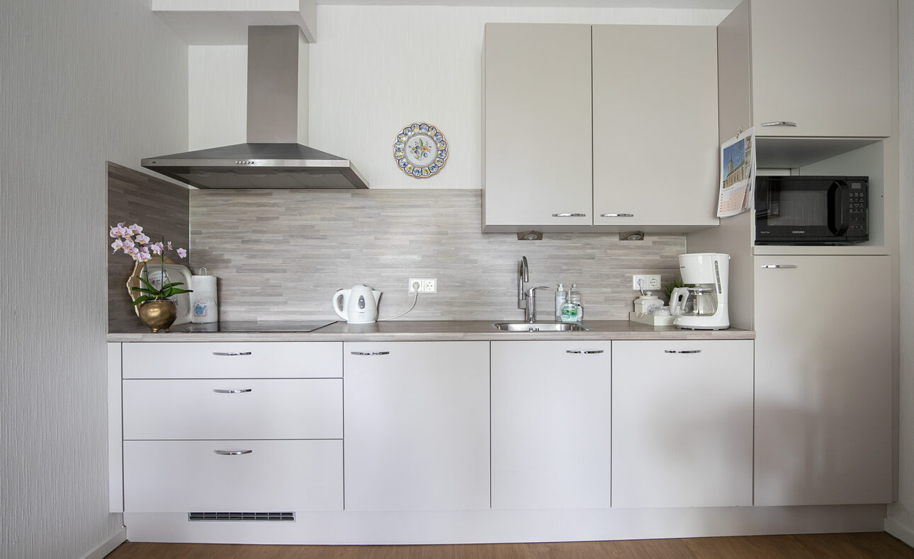 Moderne keuken met witte kasten, een magnetron, koffiezetapparaat, waterkoker en een plant op het aanrecht.