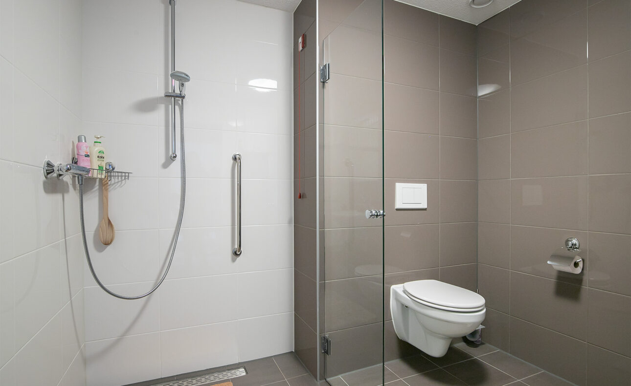 Moderne badkamer met inloopdouche, glazen wand, en hangend toilet. Neutrale kleuren en minimalistisch ontwerp.