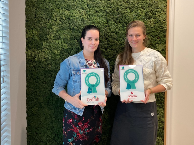 Twee vrouwen poseren met certificaten voor een groene moswand. De certificaten hebben de logo's van Cedrah en Salem.