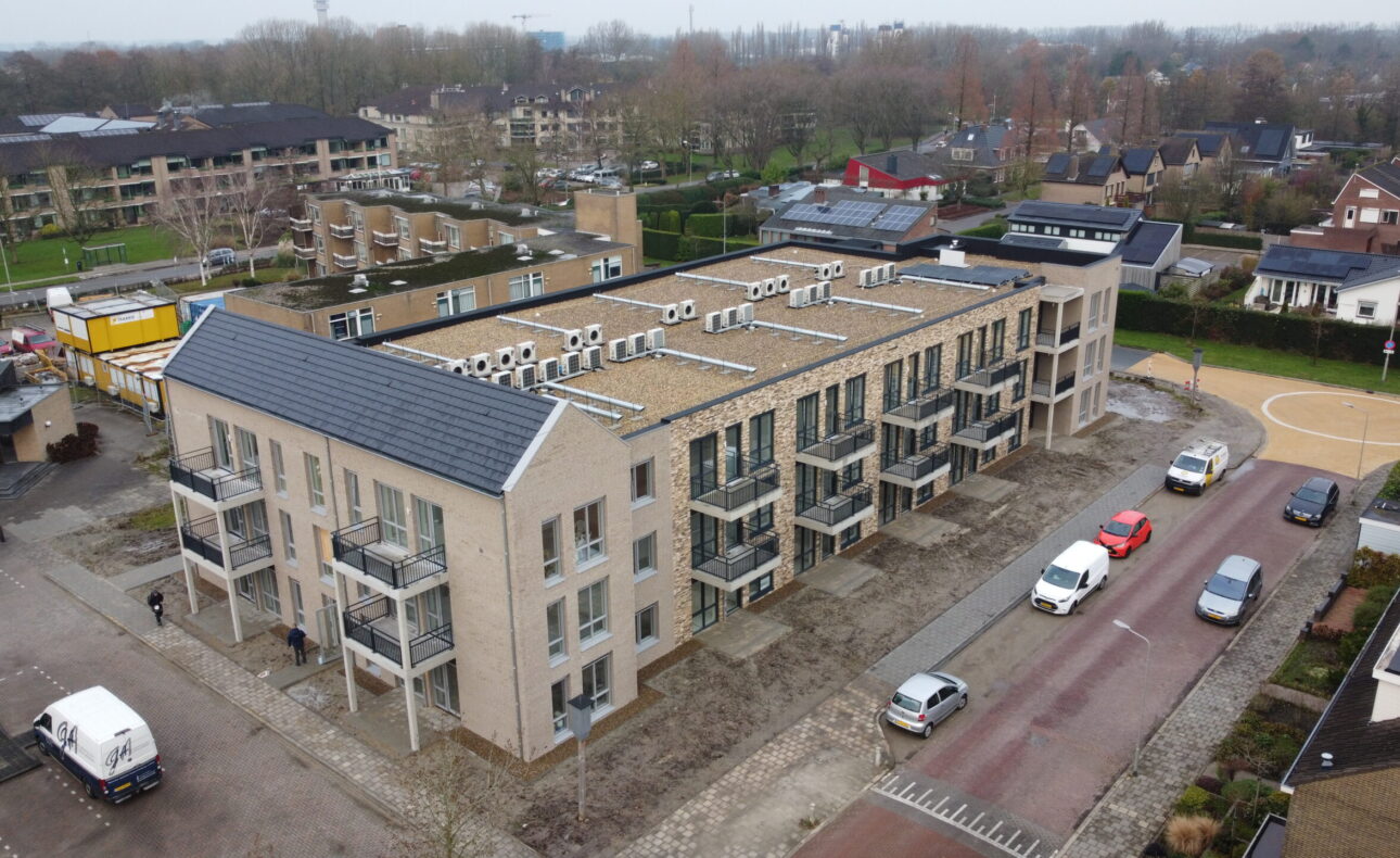 Luchtfoto van een modern appartementencomplex met meerdere verdiepingen, omgeven door geparkeerde auto's en groenvoorzieningen.