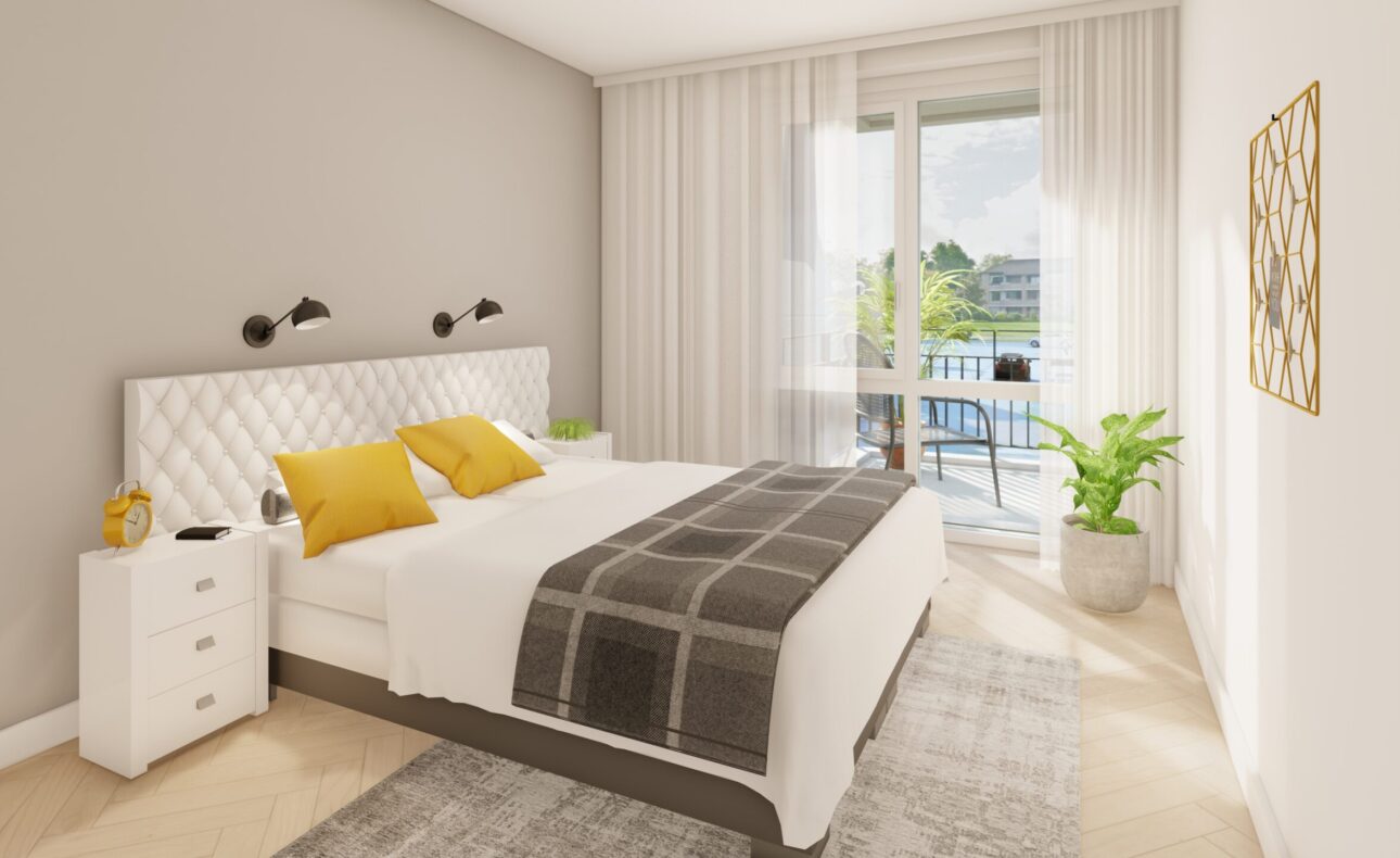 Slaapkamer met een groot bed, witte en gele kussens, nachtkastje, plant en een raam met uitzicht op een balkon en groen.