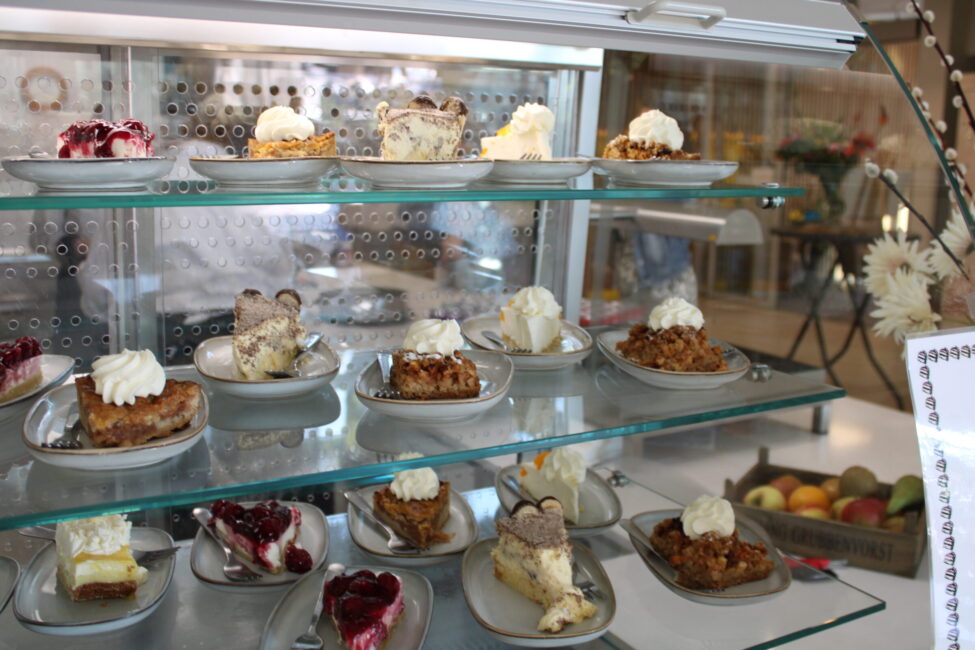 Een vitrine met verschillende soorten taart, elk geserveerd op een bordje met een toefje slagroom, in een café of bakkerij.