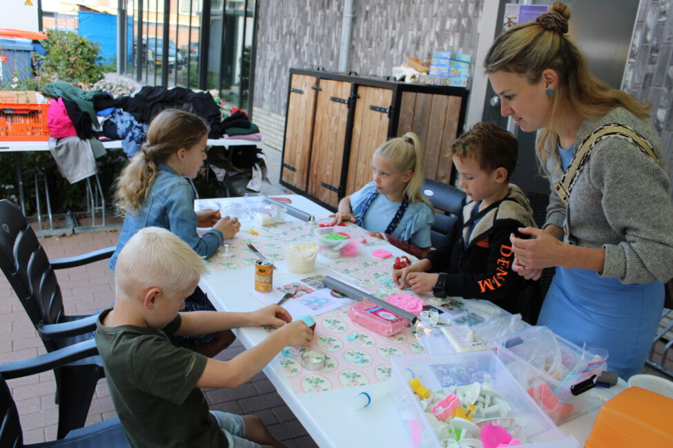 Kinderen knutselen aan een tafel onder begeleiding van een volwassene. De tafel is bedekt met knutselmaterialen en papier.