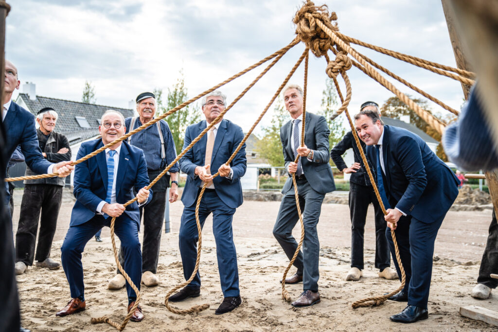 Mannen in pakken trekken aan touwen tijdens een buitenactiviteit. Ze lijken samen te werken aan een gemeenschappelijk doel.