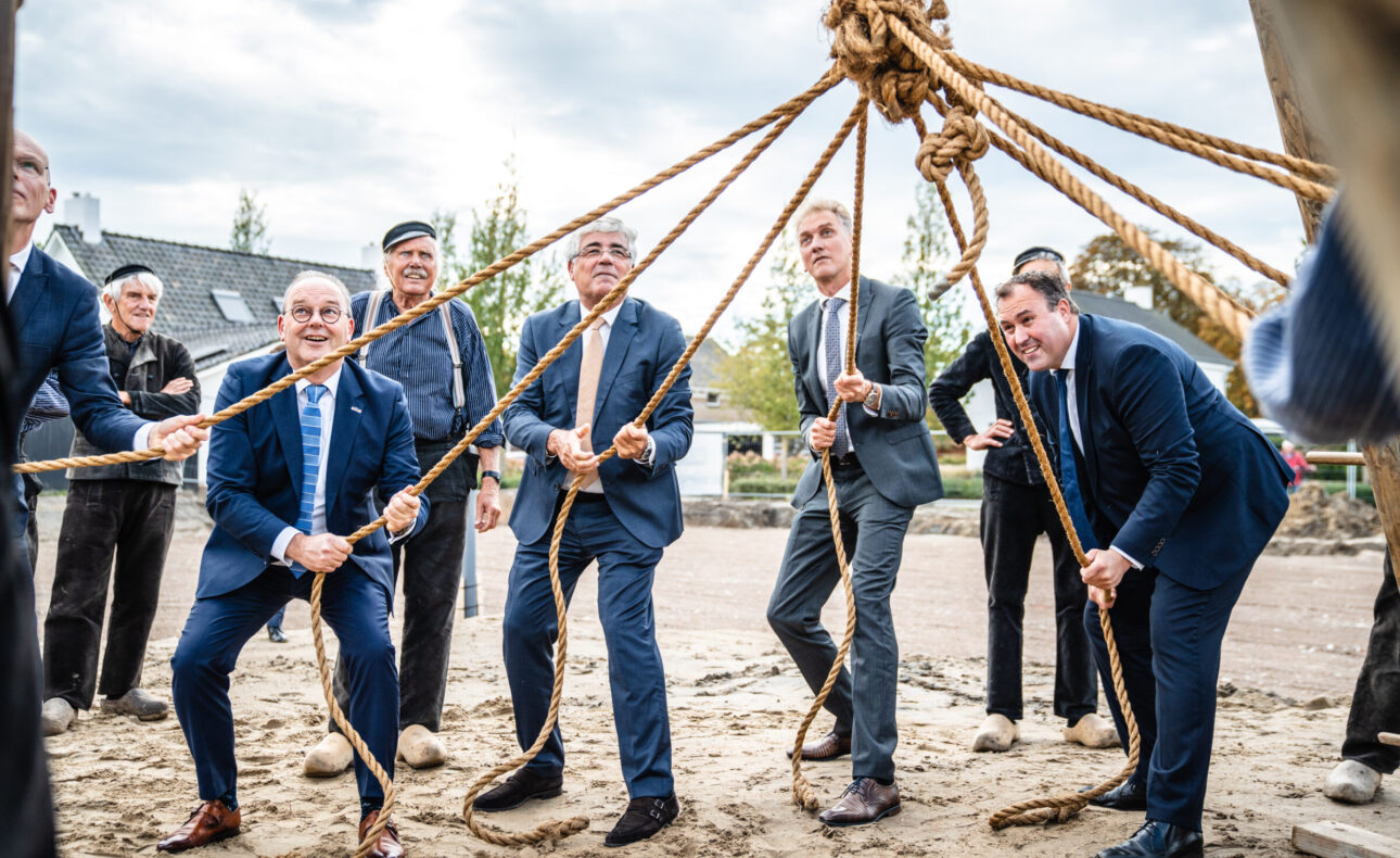 Mannen in pakken trekken aan touwen tijdens een buitenactiviteit. Ze lijken samen te werken aan een gemeenschappelijk doel.