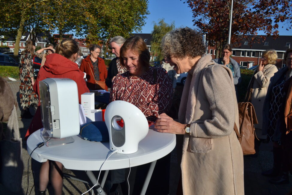 Mensen verzamelen zich rond een tafel met elektronische apparaten tijdens een zonnig evenement in de buitenlucht.