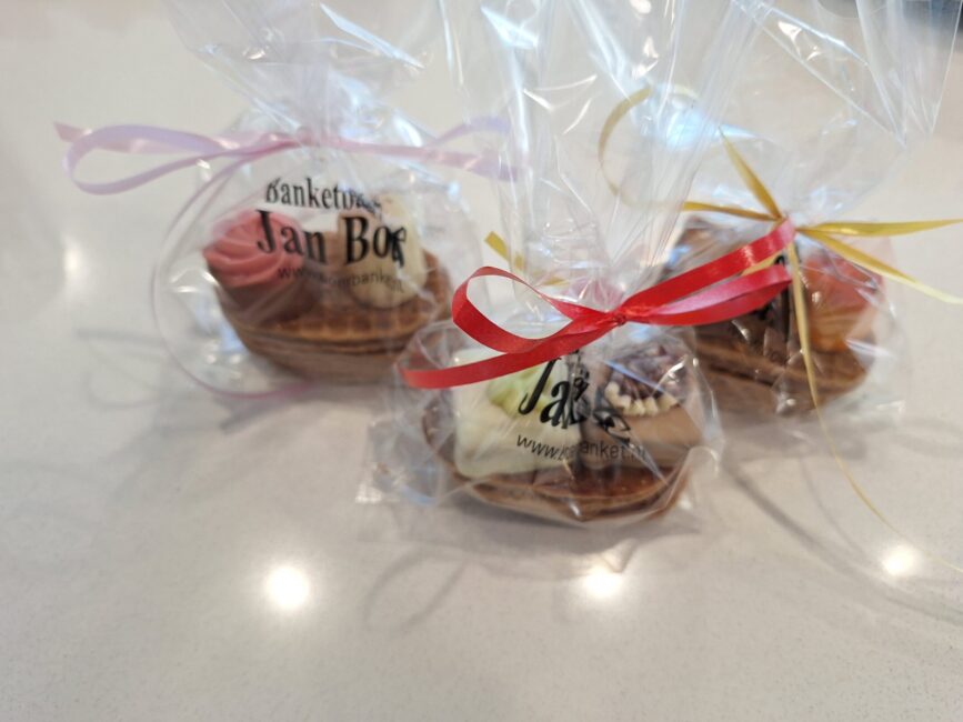 Drie verpakte gebakjes met kleurrijke linten op een tafel, klaar om uitgedeeld te worden tijdens een evenement.