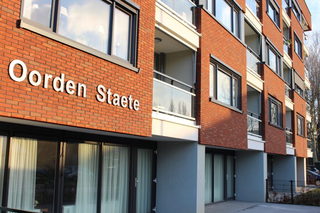 Afbeelding van de buitenkant van een modern appartementencomplex met de naam "Oorden Staete" op de gevel.