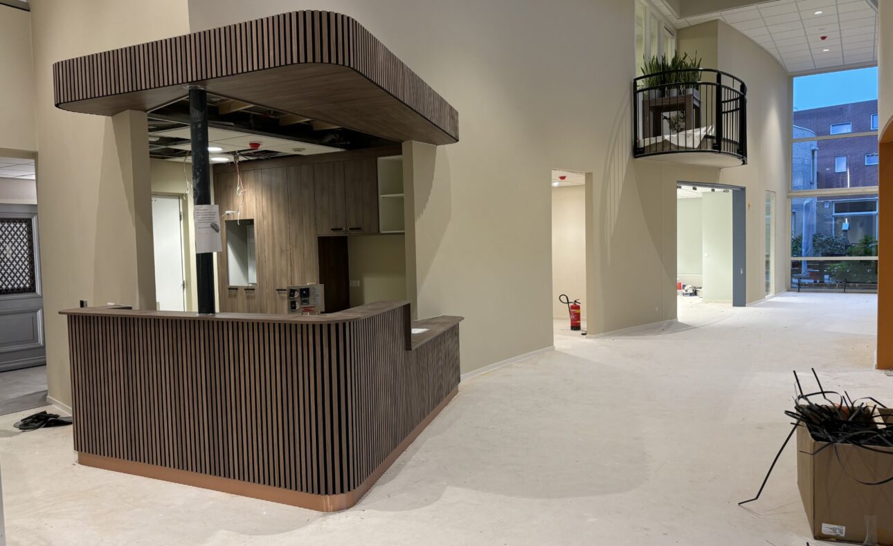 Een moderne, lege ruimte met een houten balie en lichte muren. Er is een open deur en een doos met kabels op de vloer.