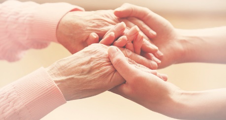 Twee paar handen houden elkaar vast, symboliserend zorg en steun. De ene hand is van een oudere persoon, de andere jonger.