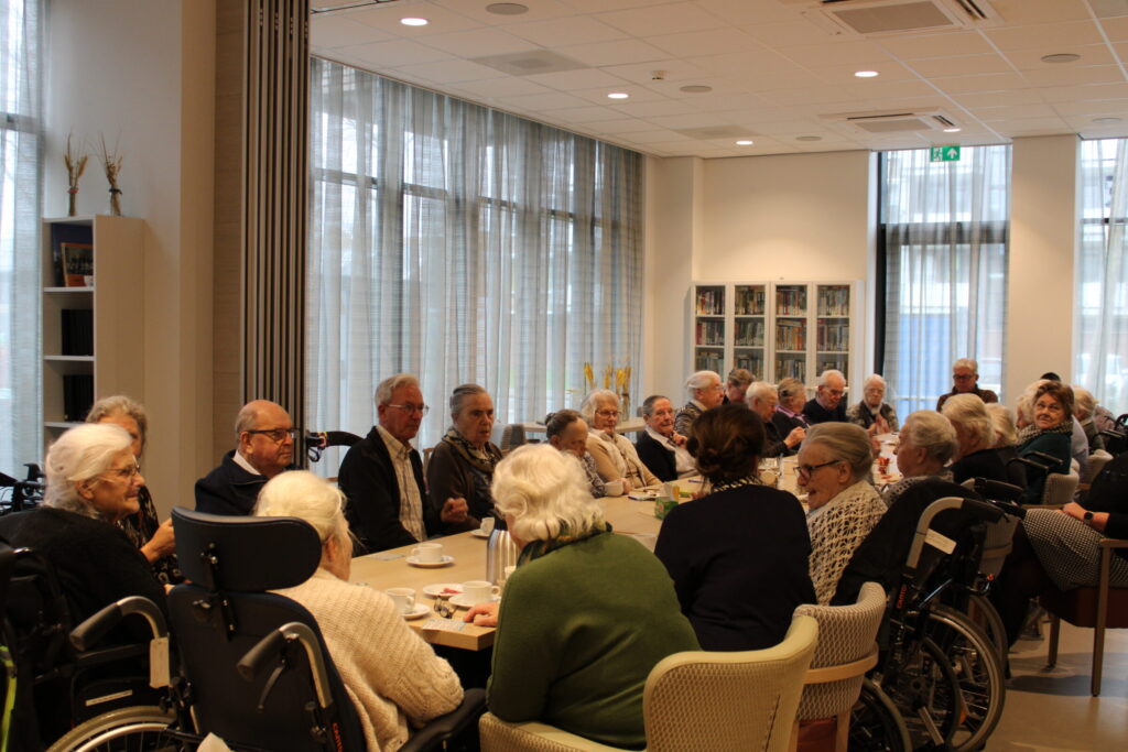 Een grote groep oudere mensen zitten rondom een tafel.