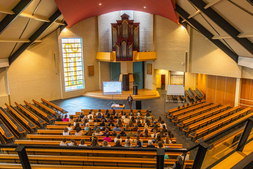 Mensen zitten in een kerk, voorin houdt een man een presentatie.