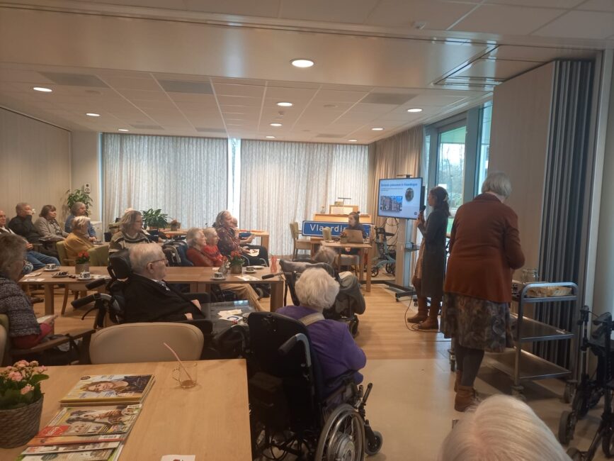 Een vrouw houdt een presentatie voor een zaal ouderen.