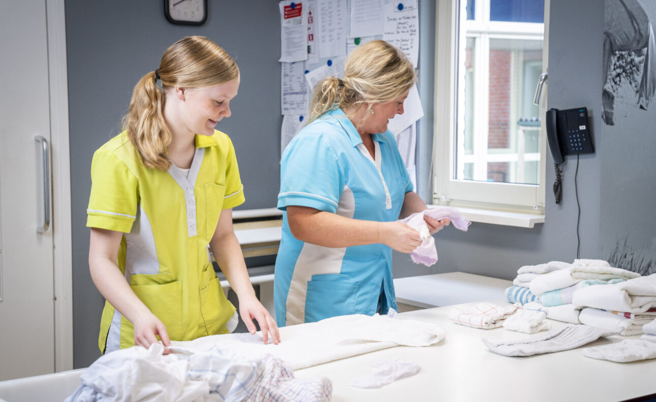 Twee huishoudelijk medewerkers die samen de was opvouwen.
