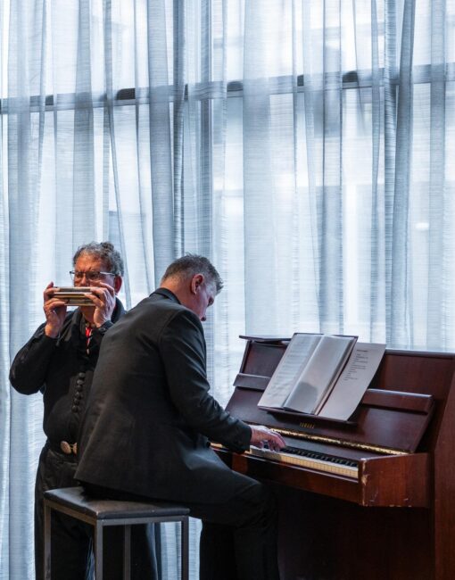Een man speelt piano, een andere man speelt mondharmonica.