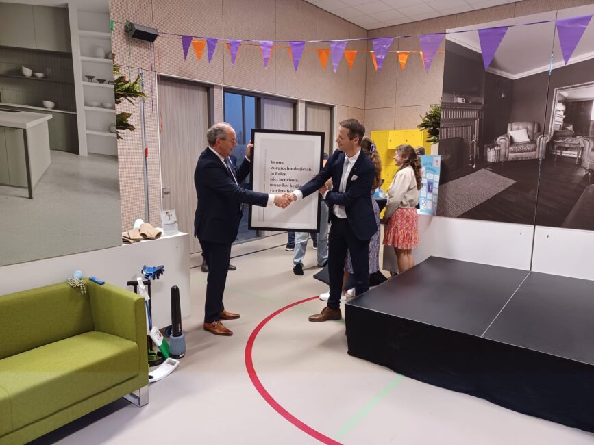 Twee mannen houden een groot rechthoekig bord vast en feliciteren elkaar tegelijkertijd.