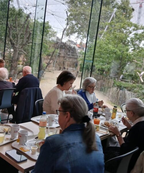 Mensen zitten aan een tafel te eten, op de achtergrond is een volière te zien.