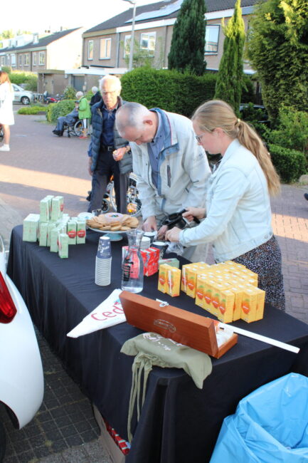 Een tafel met pakjes drinken en bekertjes, daarachter staan een man en een vrouw die koffie inschenken.