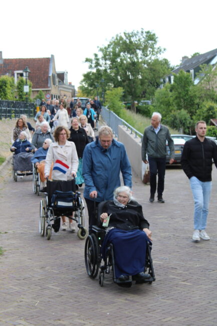 Een optocht van rolstoelen die worden geduwd en mensen die meelopen door een straat.