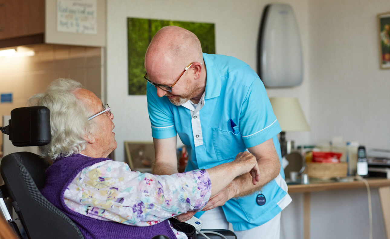 Een mannelijke medewerker helpt een vrouw in een rolstoel.