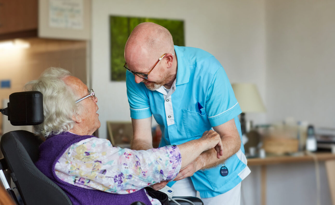 Een medewerker helpt een bewoner in een stoel
