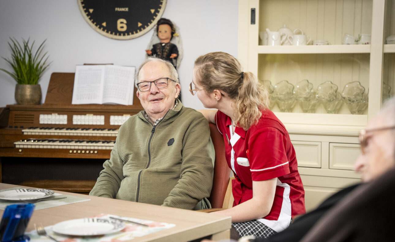 Zorgmedewerker zit aan tafel met een bewoner
