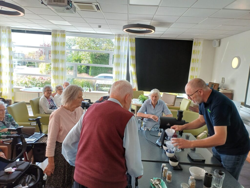 Ouderen staan voor een tafel te kijken naar een demonstratie.