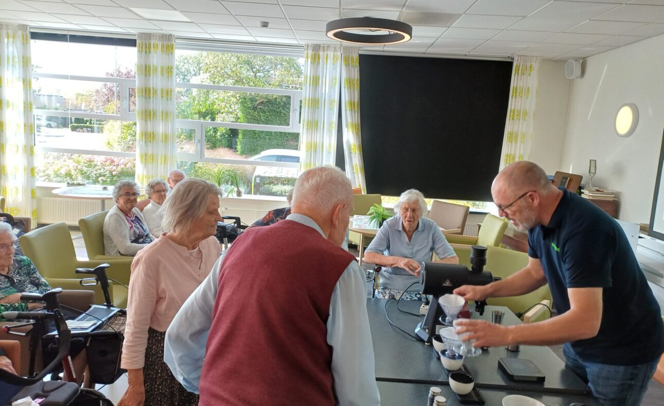 Ouderen staan voor een tafel te kijken naar een demonstratie.