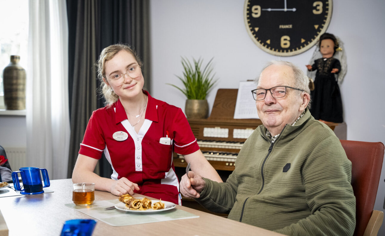 Een zorgmedewerker en een bewoner zitten aan tafel,