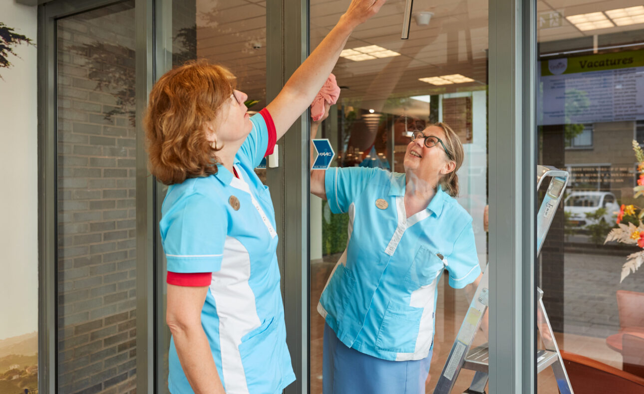 Twee medewerkers maken een glazen deur schoon.