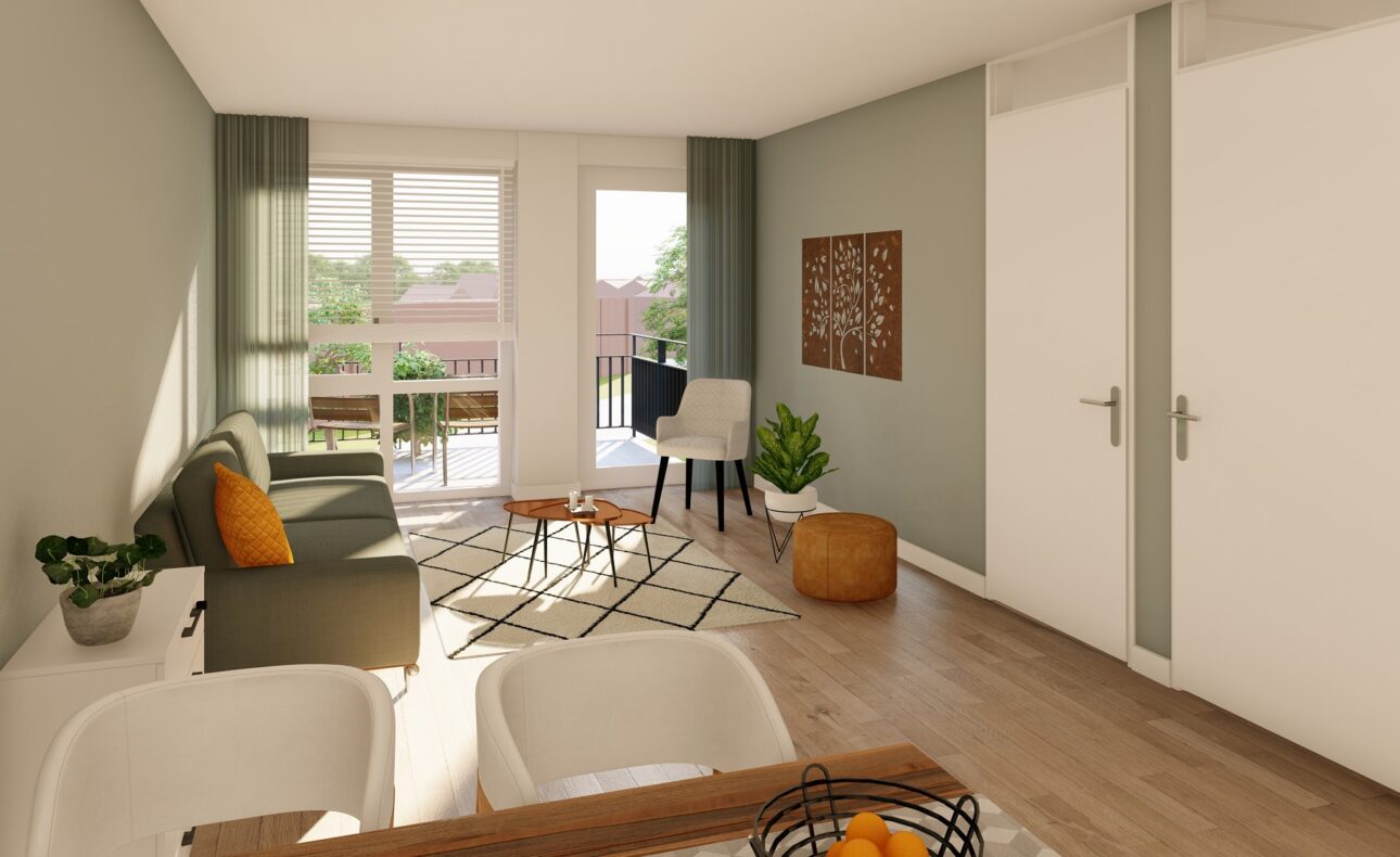 Op de foto is de woonkamer van één van de appartementen te zien. In de woonkamer staat een bank, fauteuil en een deel van de zithoek is te zien. Er zijn hoge ramen in de woonkamer waardoor er veel licht binnenvalt. Vanuit de woonkamer is er toegang tot het balkon.