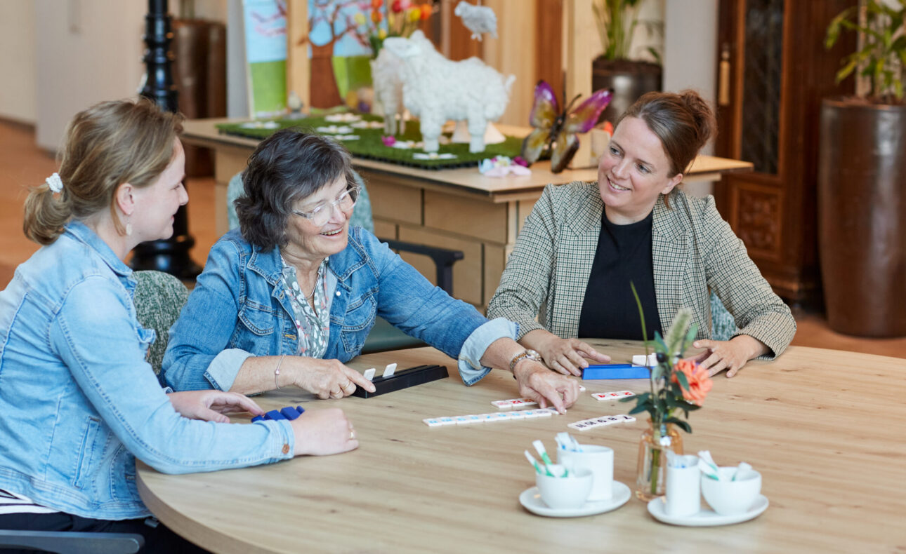 Medewerkers spelen een spelletje met een bewoner.
