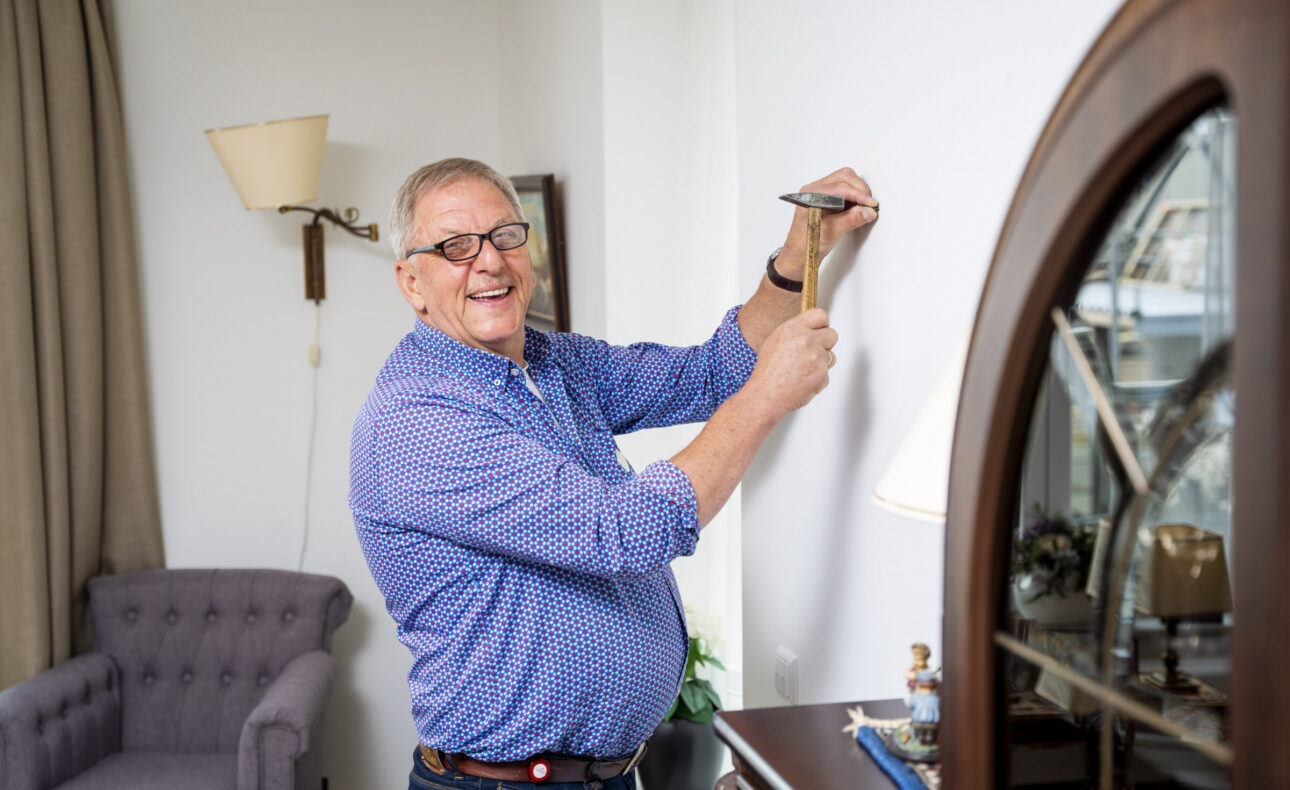 Een medewerker slaat een spijker in de muur om wat op te hangen.
