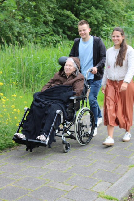 Twee jongeren duwen een oudere dame in een rolstoel