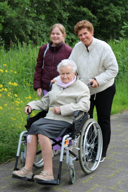 Een vrouw en een meisje duwen een oudere dame in een rolstoel