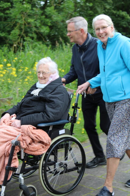 Een man en een vrouw duwen een oudere dame in een rolstoel