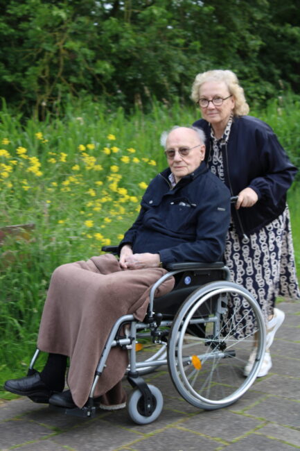 Een oudere man in een rolstoel wordt geduwd door een vrouw.