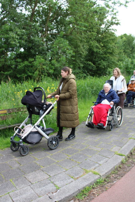 Een vrouw met een kinderwagen en daarachter een oudere dame in een rolstoel die wordt geduwd.