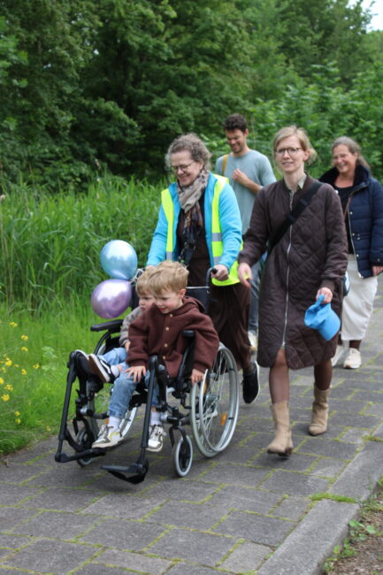 Twee vrouwen lopen achter een rolstoel met daarin twee kleine jongetjes