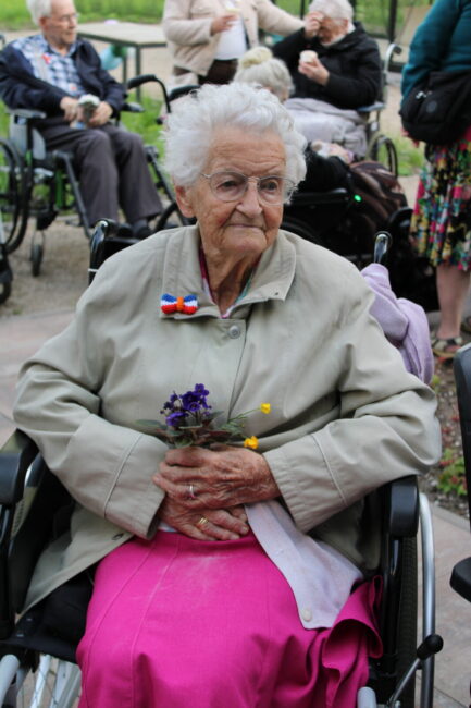 Oudere dame in rolstoel met bloemen in haar hand en speldje op